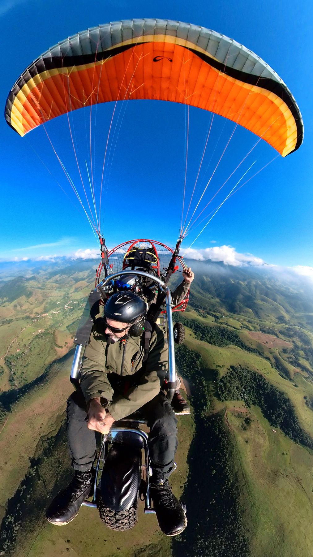 Paramotor with an orange wing over the mountains