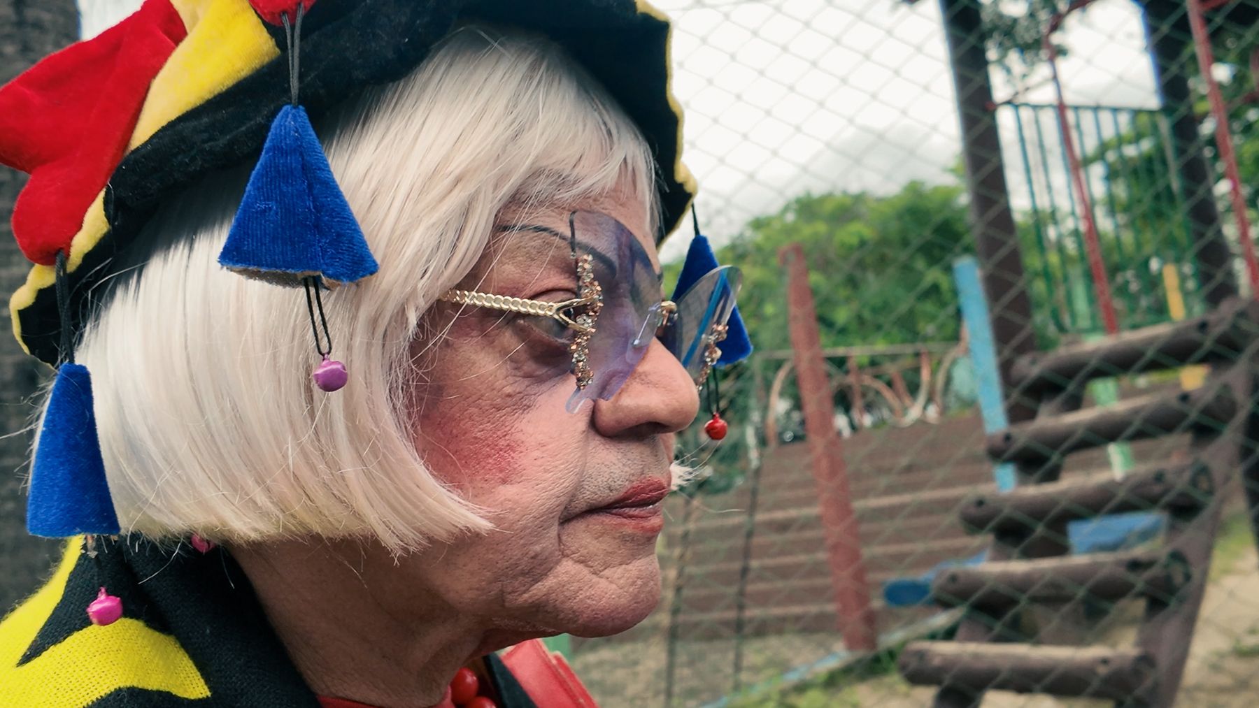 Gui-Gui in profile, white wig, jester hat with blue tassels and jewelled glasses