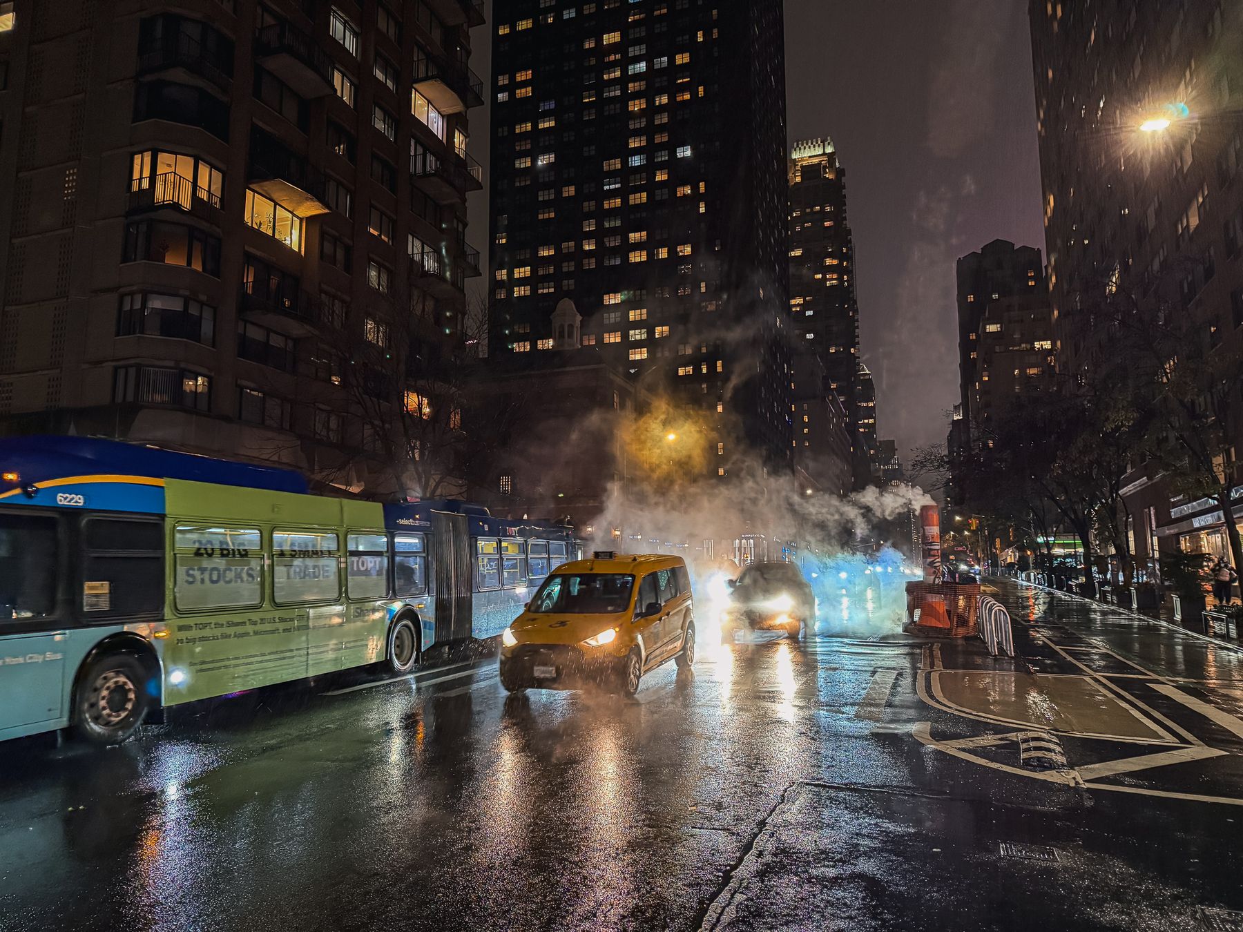 Bus and yellow cab on a wet avenue at night, New York