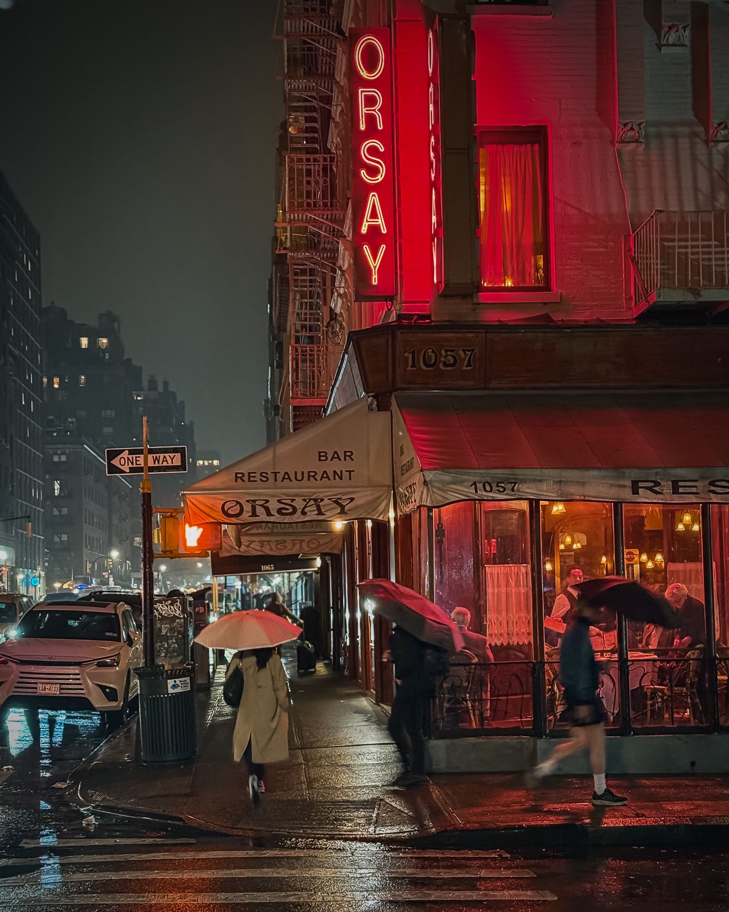Orsay restaurant corner with red neon on a rainy night, New York
