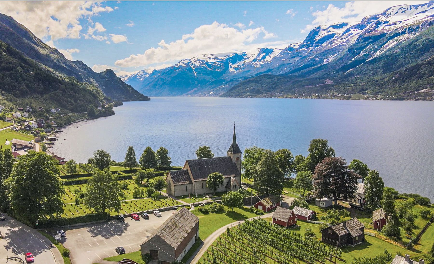 Village with a white church by the fjord, snowy mountains behind, Norway